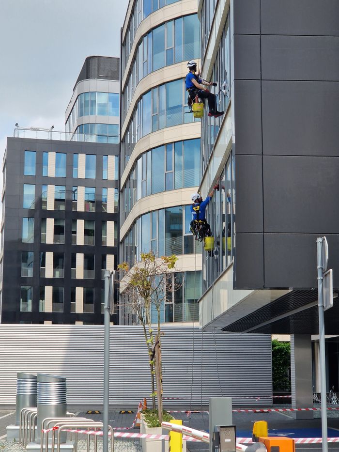 about-02 Two workers clean windows on a tall office building in a city setting.